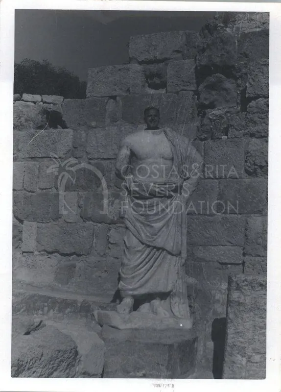 A man stands behind a draped marble statue in front of a large stone block wall