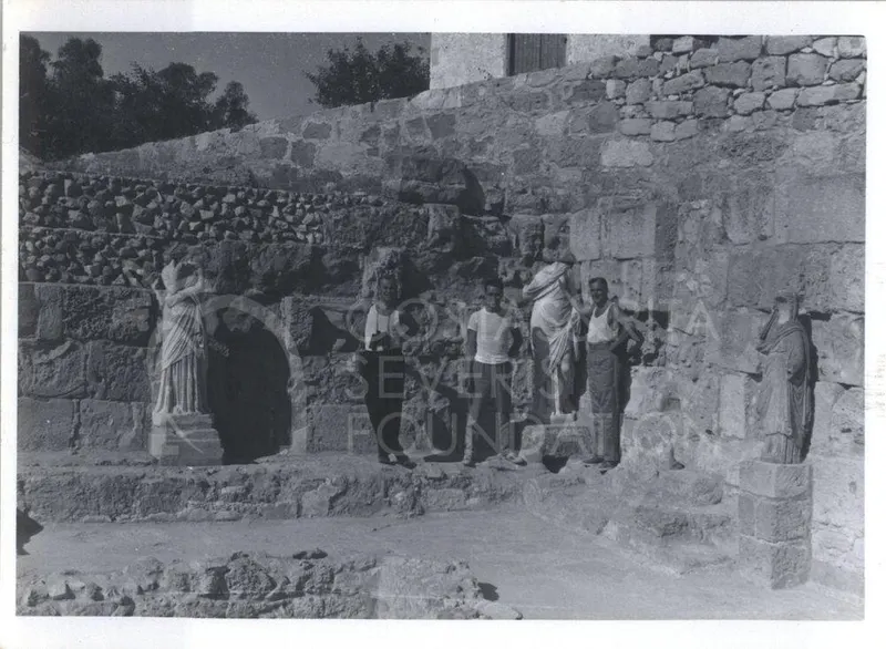 Three men pose among draped statues against a stone wall at Salamis