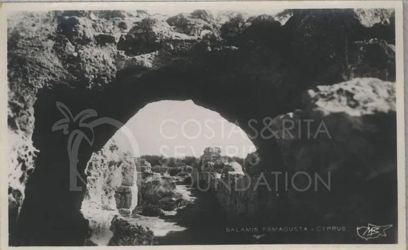 Ruined walls of Salamis seen through a rock arch, with a path leading between them under a pale sky