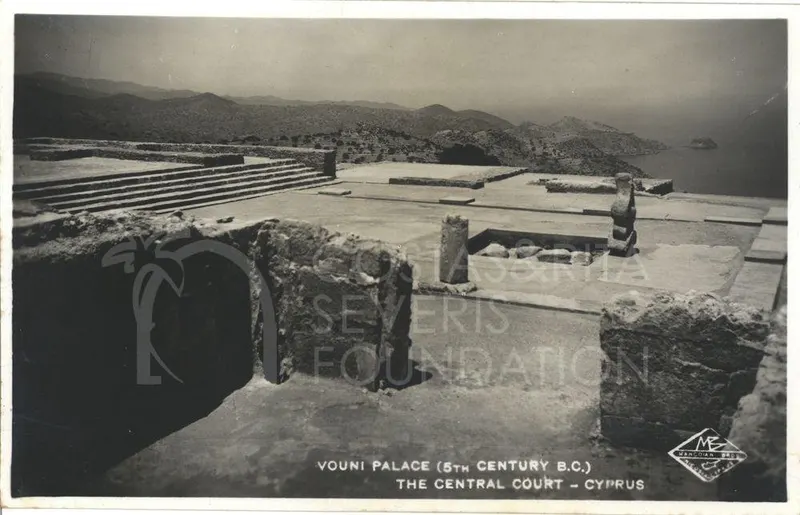 Stone-paved central court of Vouni Palace with low walls, a standing column and hills and sea beyond