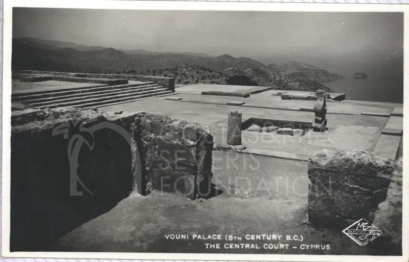 Ruined central court of Vouni Palace with stone steps, low walls and a column, with hills and sea behind