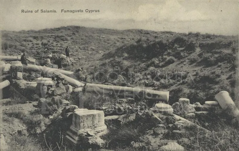Fallen column drums and broken blocks scattered on a grassy slope at Salamis, with two figures among the ruins