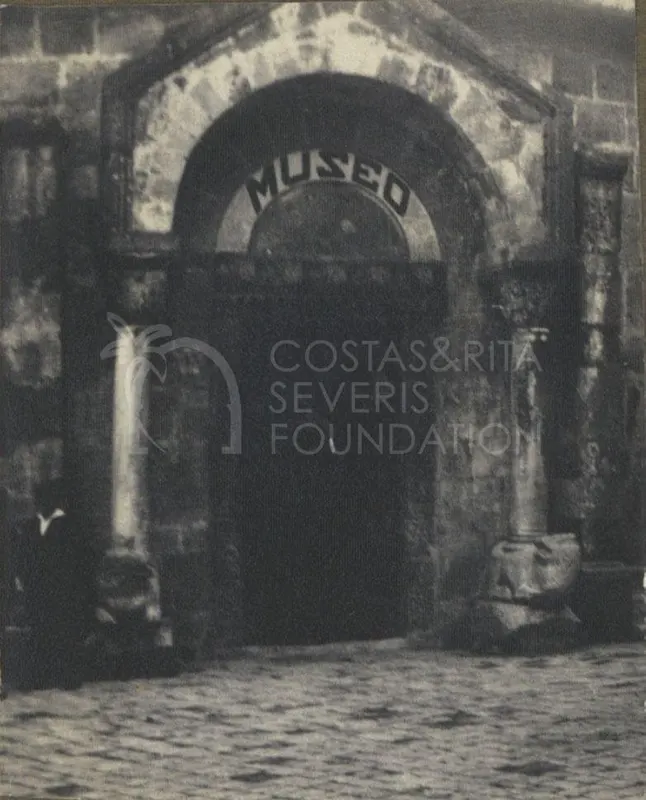 Arched stone doorway marked MUSEO, with a column on the right and a cobbled street in front