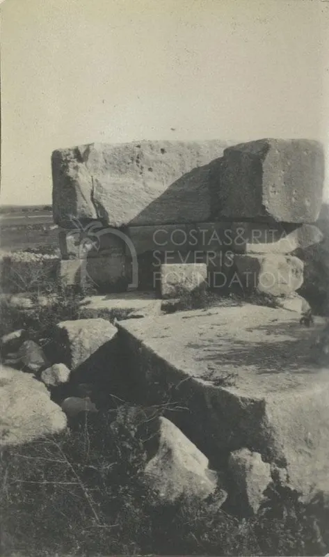 Large dressed stone blocks stacked and scattered among scrub at Palaepaphos