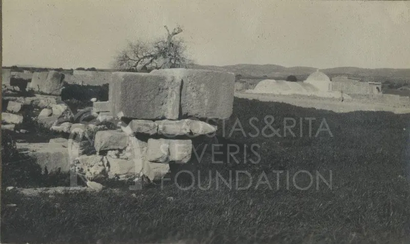 Large dressed stone blocks over rubble at Palaepaphos, with a domed building and a tree in the distance