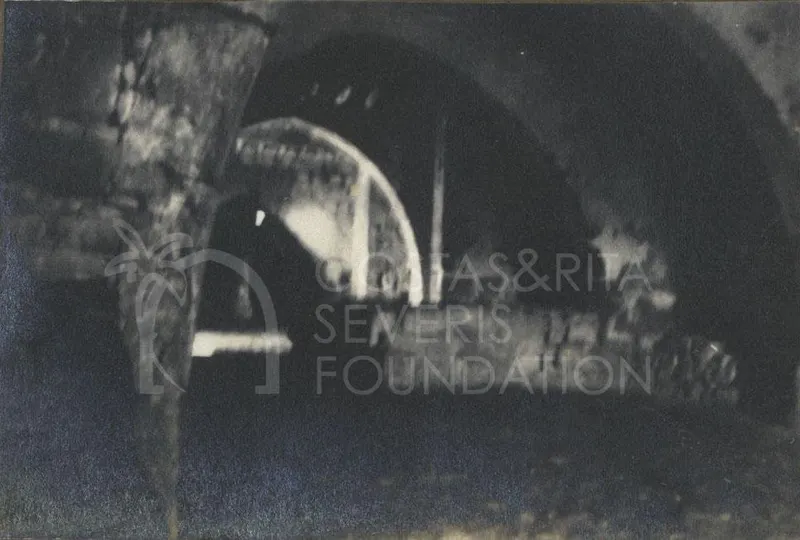 Dim view through a stone arch in a vaulted interior, with a large pillar at the left edge