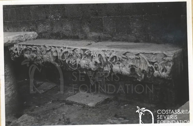 Carved stone relief block with scrolling foliage and curling forms against a dark masonry wall