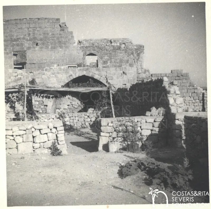 Ruined stone walls with a large arch and low rubble walls in the foreground at Kouklia