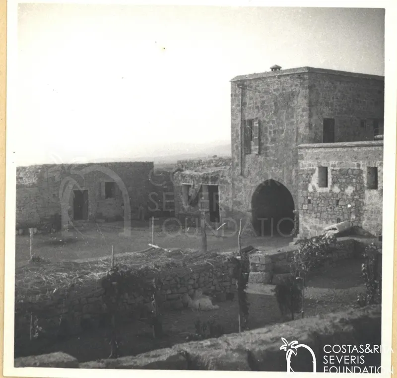 Stone buildings with an arched doorway around a dirt courtyard at Kouklia