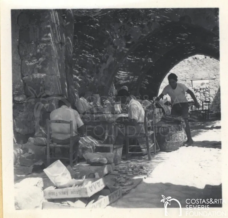 Four people work on finds under stone arches at Kouklia, with sacks and a large basket nearby.