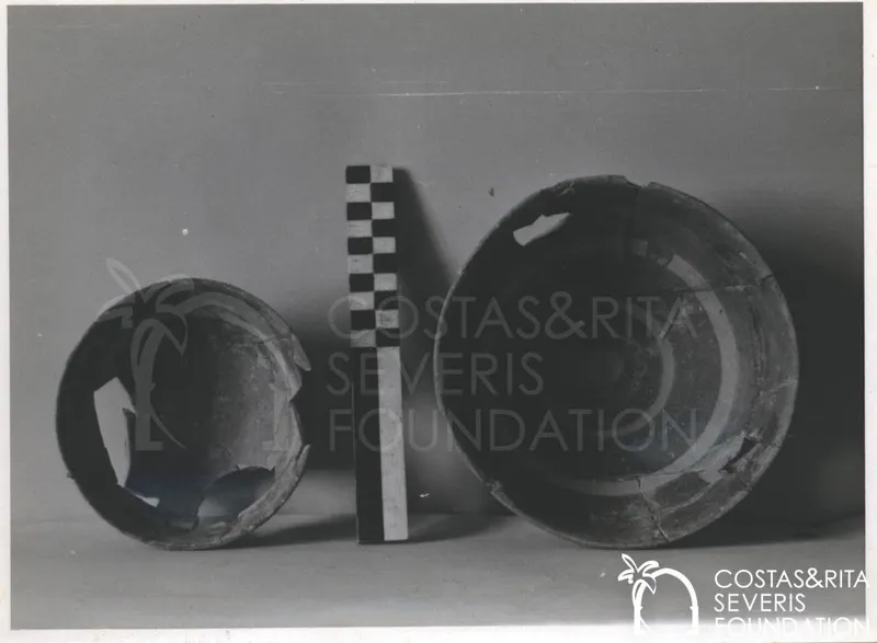 Two broken pottery bowls on a plain background, with a checkered scale bar standing between them