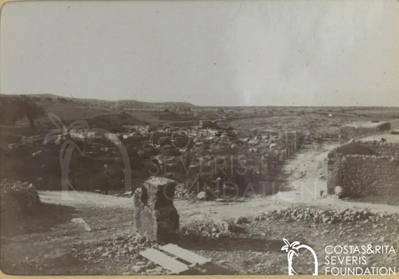 Stony slope with low houses and walls at Kouklia, with a large stone block in the foreground