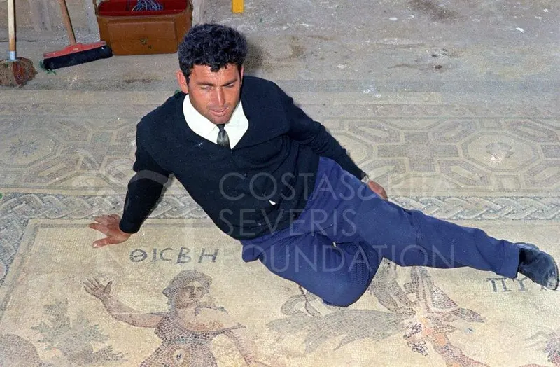 A man in a dark sweater reclines on a mosaic floor with geometric borders and figures