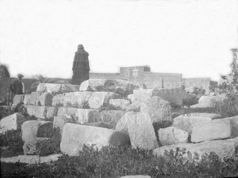 Large fallen stone blocks in grass, with a figure in a long coat standing among them