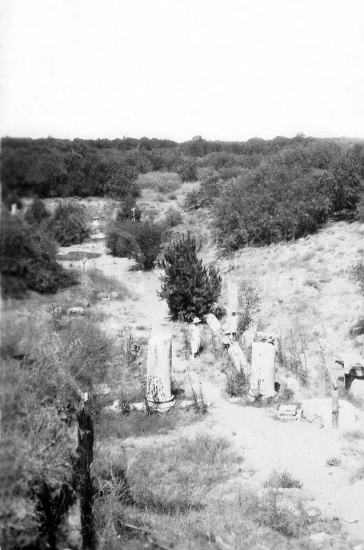 Fallen column drums among scrub on a sandy path at Salamis, with one person in a hat standing beside them