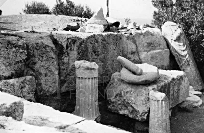 Two fluted column drums and a stone block with a mortar among ruined stone walls