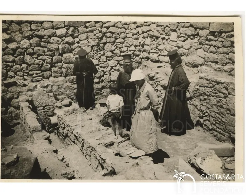 Three bearded clergymen, a woman in a white hat and a small boy stand among excavated stone walls