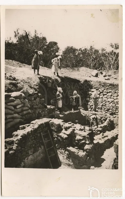 Workers dig in a deep excavation trench among stone walls, with figures standing on the rim and a ladder on the left.