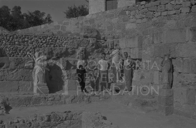 Three people pose among stone walls beside two draped marble statues at Salamis