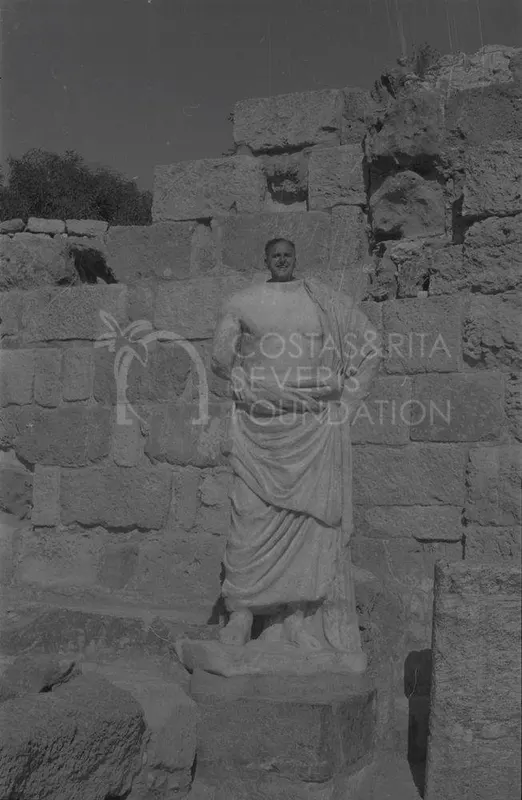A man poses behind a draped marble statue in front of a stone block wall