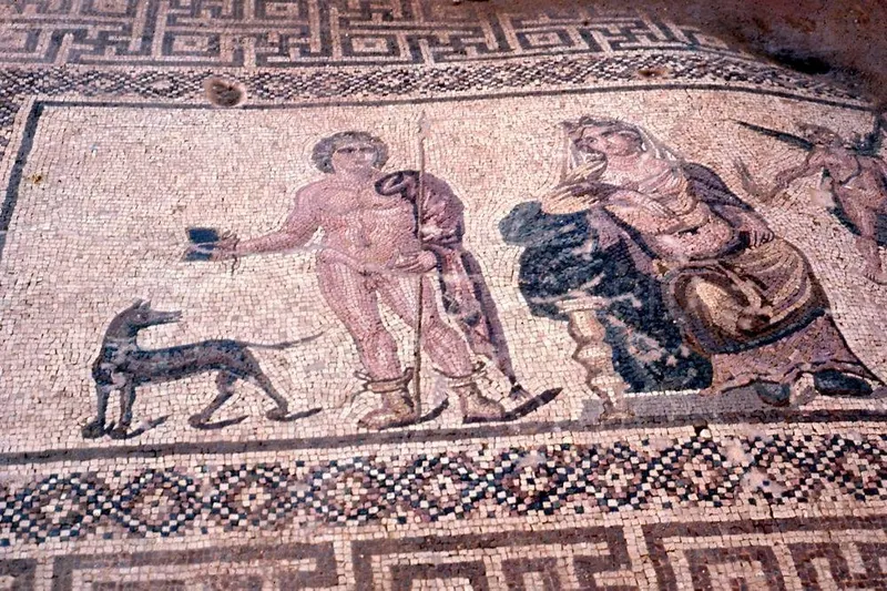 Floor mosaic with a spear-bearing figure and a dog beside a draped figure, framed by geometric borders