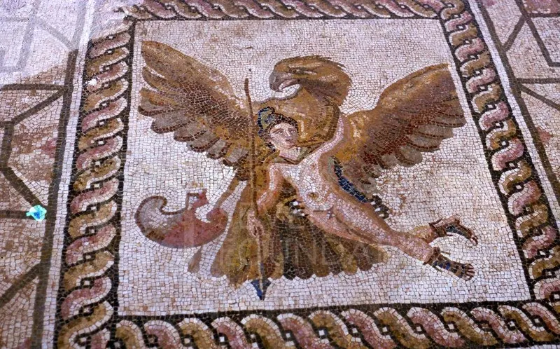 Floor mosaic of a large bird with outspread wings holding a nude figure, within a braided border