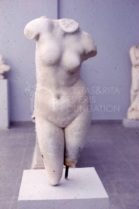 Headless marble female torso on a white pedestal in a museum gallery