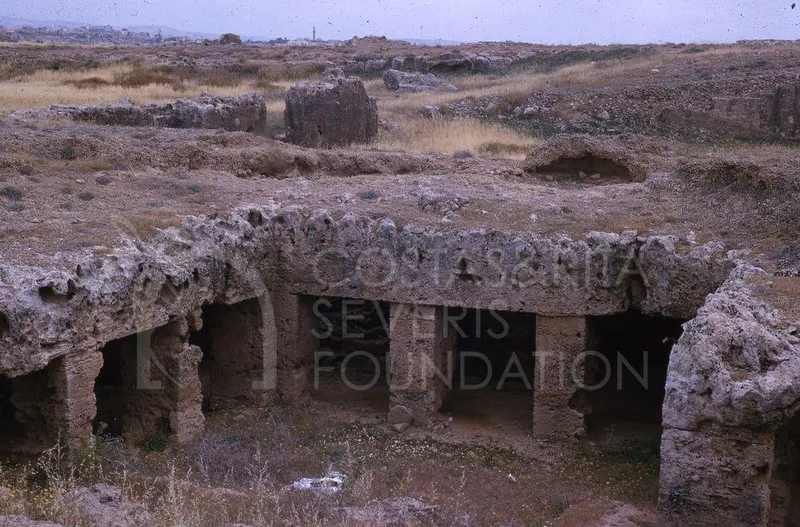 Rock-cut tomb facade with pillars and dark chamber openings in a dry, stony landscape