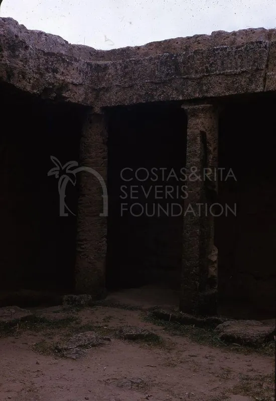 Rock-cut tomb front with two square pillars under a carved stone lintel, opening into dark chambers
