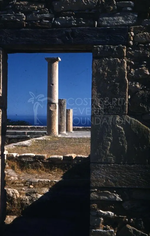 Three stone columns seen through a stone doorway, with blue sky and sea behind them