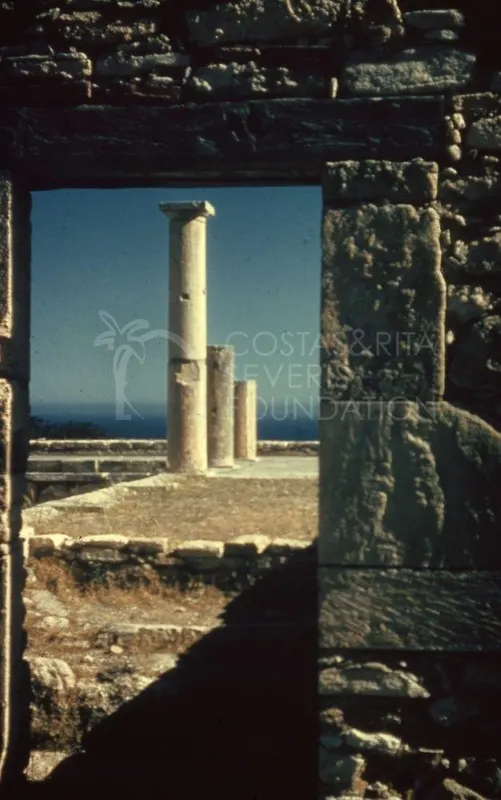 Three stone columns seen through a gap in a stone wall, with the sea on the horizon