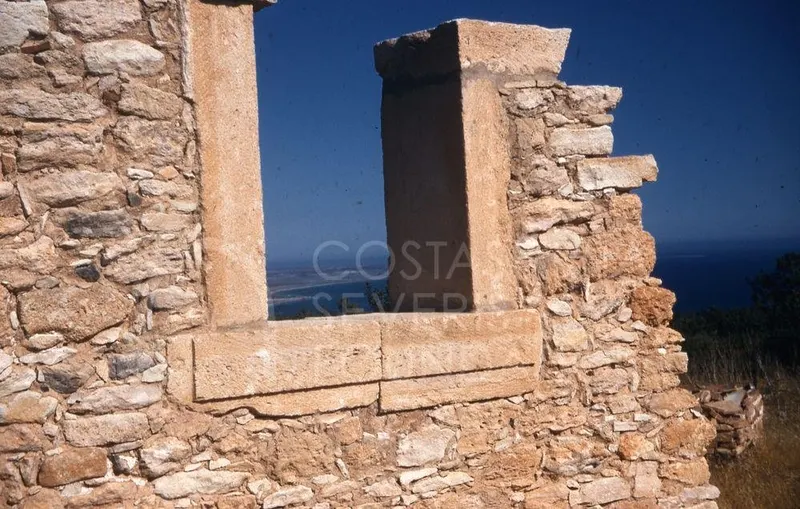 Ruined stone wall with a rectangular opening framing a view of the sea and coastline