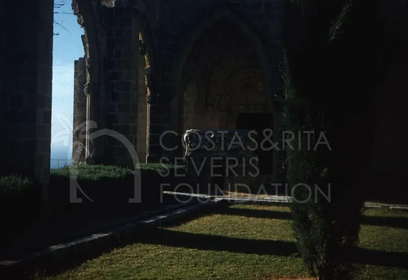 Carved stone sarcophagus in an arched passage of Bellapais Abbey, with grass and a cypress tree in front