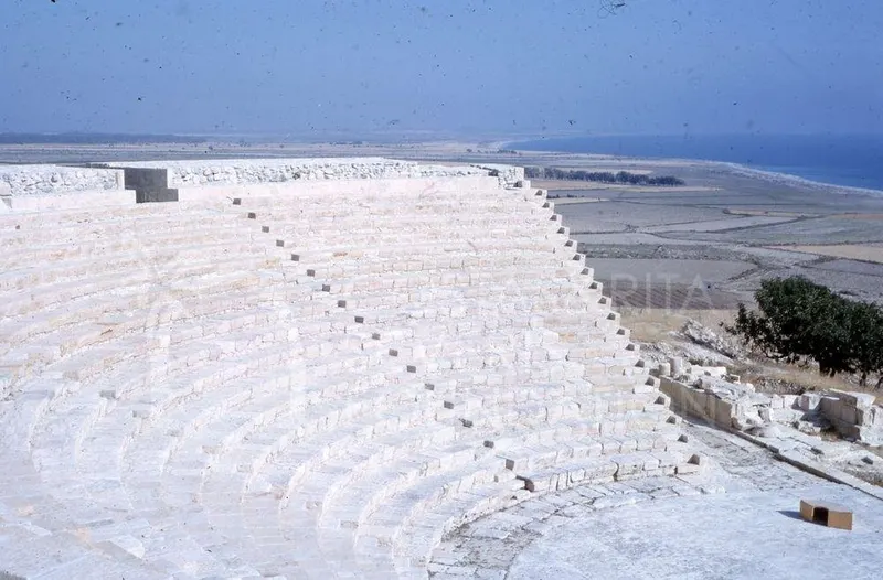 Curved white stone tiers of the theatre at Kourion, with flat land and sea beyond