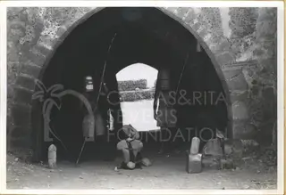 Two men in improvised costumes stand under a stone archway, one holding a long pole