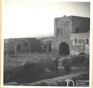 Stone buildings with an arched doorway around a dirt courtyard at Kouklia