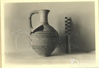 Handled jug with banded body beside a chequered scale rod