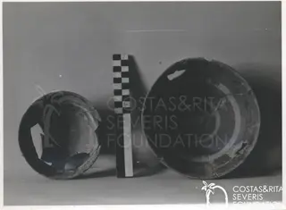 Two broken pottery bowls on a plain background, with a checkered scale bar standing between them