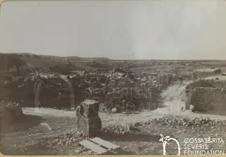 Stony slope with low houses and walls at Kouklia, with a large stone block in the foreground