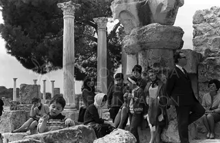 Visitors and children among stone ruins at Salamis, with columns and a carved capital behind them under a pine tree