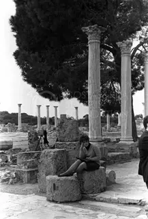 Woman seated on a stone block among columns at Salamis, with a camera on a tripod nearby