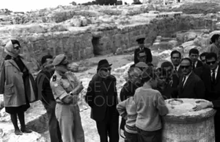 Group of visitors and a uniformed man among ancient stone ruins, with a carved stone block at right