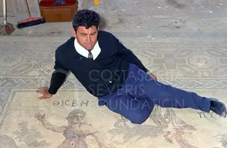 A man in a dark sweater reclines on a mosaic floor with geometric borders and figures