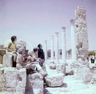 Five people sit and stand on ancient stone blocks, looking up at a row of columns at Salamis
