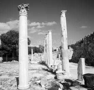 Row of tall ancient columns with carved capitals across a paved court, with fallen stone blocks in the foreground