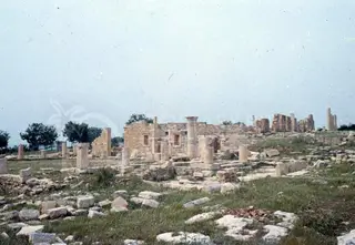 Ruined stone columns, walls and scattered blocks of the Sanctuary of Apollo Hylates on a grassy hill