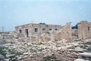 Stone ruins with a low building with small windows and fallen blocks in the foreground