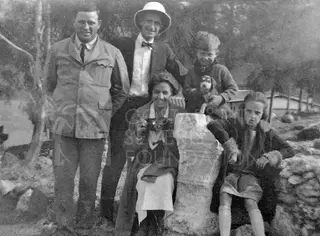 Five people and a small dog posing outdoors beside a large stone pillar