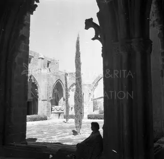 Seated woman in a dark archway looking out over the ruined courtyard of Bellapais Abbey