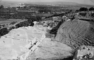 Ruins of the amphitheatre of Soloi on a hillside, with a wide valley of fields and trees beyond